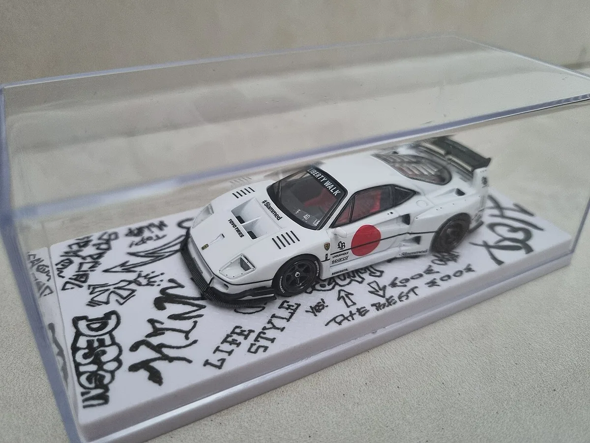 Een witte modelraceauto met zwarte opschriften staat op een witte sokkel in een doorzichtige acrylaten stolp met vlakke zijden.