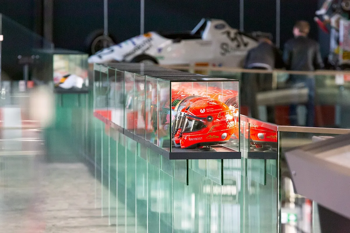 Een rij glazen vitrinekasten in een automuseum; in een van de kasten ligt een rode helm die van bovenaf wordt aangelicht.