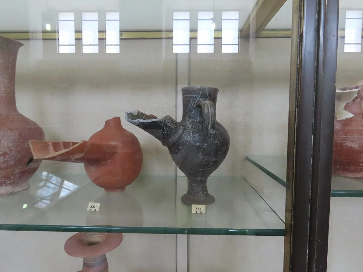 Close-up van glazen legplanken in een museumvitrine met aardewerken kruiken en schalen erop, gezien door het zijglas van de kast.