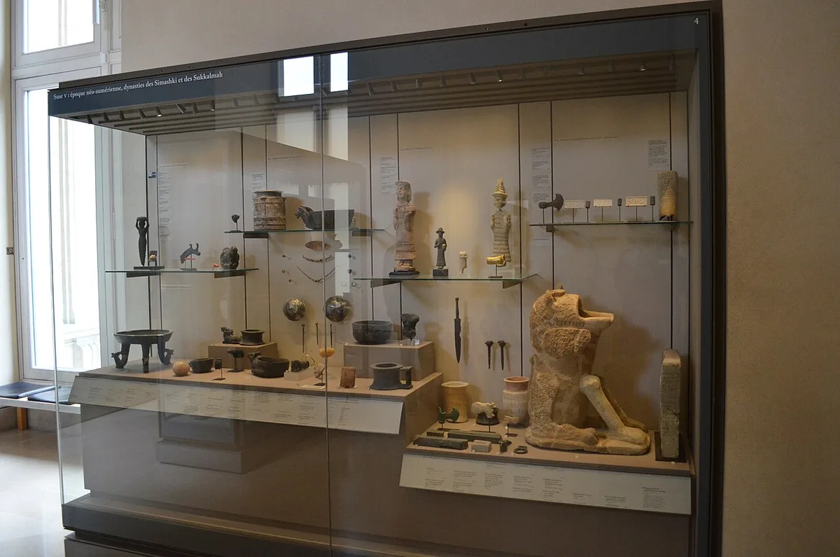 Een grote gesloten museumvitrine met schuifpanelen van glas, gevuld met archeologische voorwerpen op meerdere glazen legplanken.