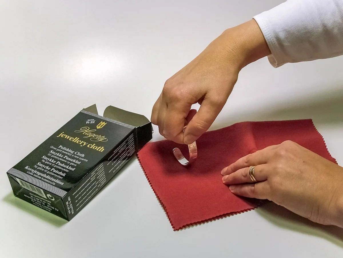 Twee handen halen een rode poetsdoek uit een groen doosje met het opschrift jewellery cloth, op een witte ondergrond.